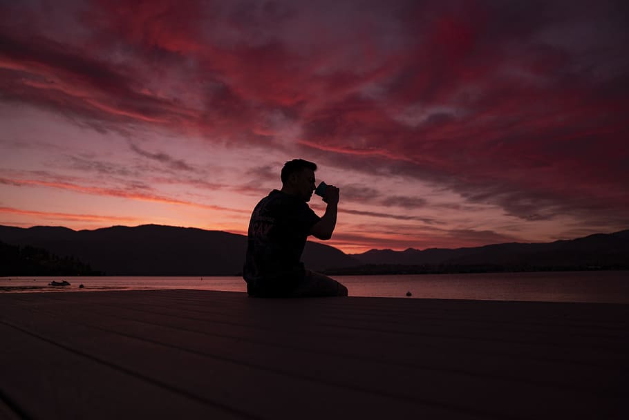 man sitting on dock during golden hour, silhouette, red, sky