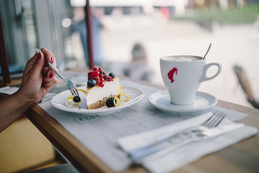 Woman Enjoying Cheese Cake and a Coffee with Fruits in a Cafeteria