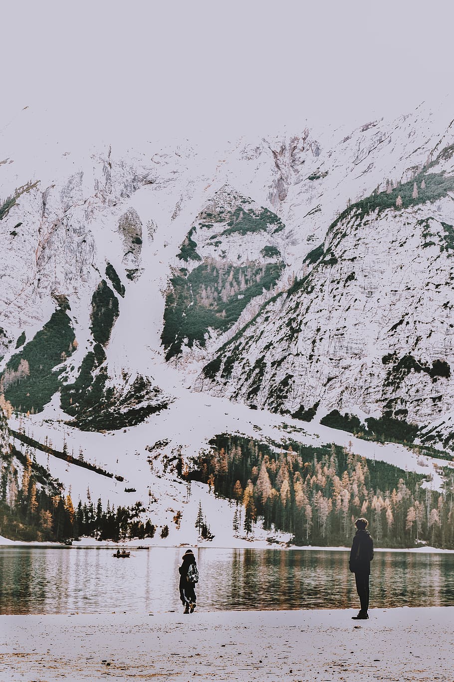 Two People Standing on Shore Overlooking Body of Water and Snow Covered Mountain HD wallpaper