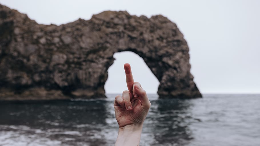 person showing right middle finger on front of brown rock formation, HD wallpaper