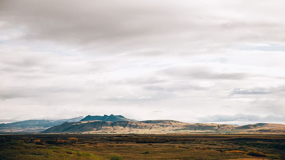 Panoramic view of gray cloudy sky over the vast field with mountains in the background HD wallpaper