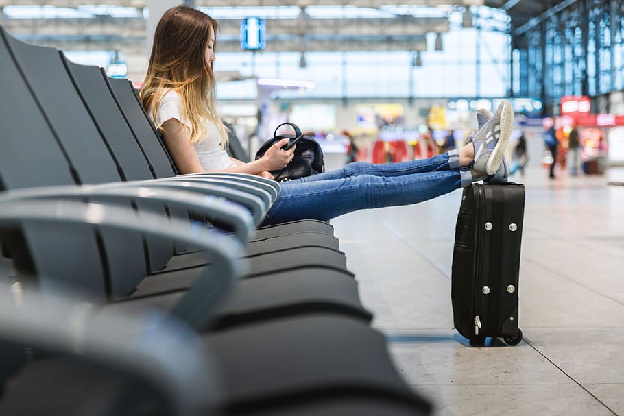 Young girl with long hair is sitting in airport. She put her legs on suitcase near. HD wallpaper