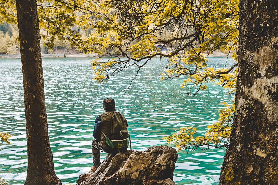 Photo of Man Sitting on Rock Near Lake, back, backpack, backpacker HD wallpaper