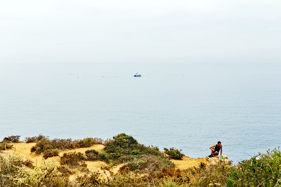 Man Sitting On Cliff, coast, horizon, lagos, nature, ocean, ponta da piedade, HD wallpaper
