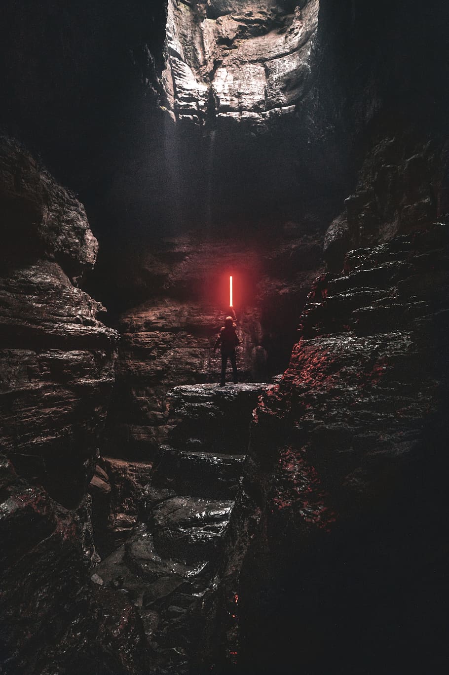 man holding red lightsaber standing on cliff, person, cave, glow
