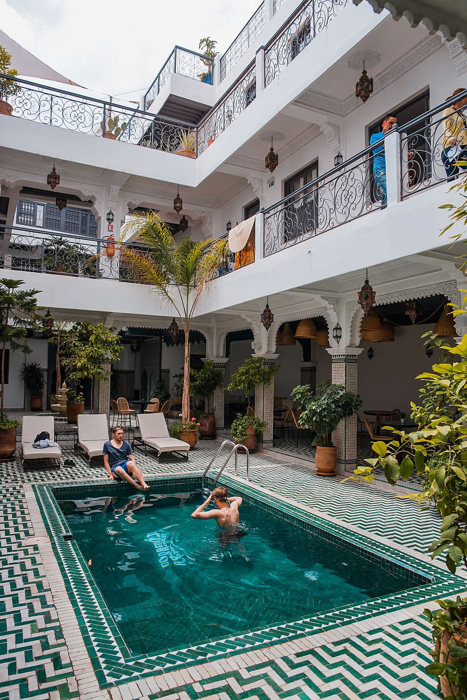 two men on pool beside three beige loungers, plant, marrakesh