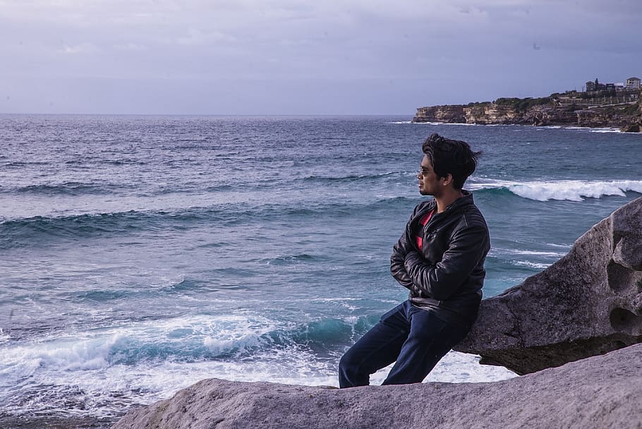 Man Leaning on Rock Near Beach Shore, black leather jacket, boulder HD wallpaper