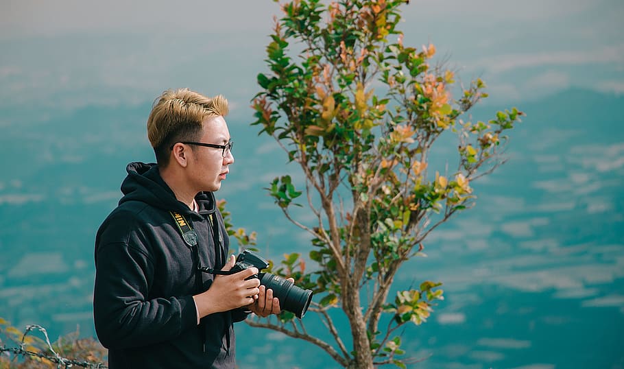Man in Black Jacket in Front Green Plant, camera, daytime, holding HD wallpaper