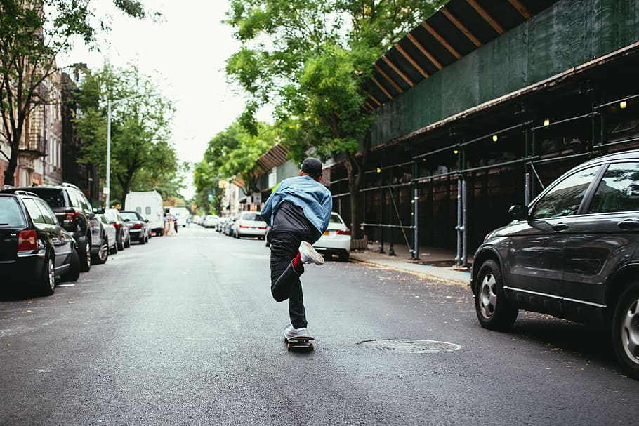 A young caucasian skateboarder wearing black cap skateboarding in the street