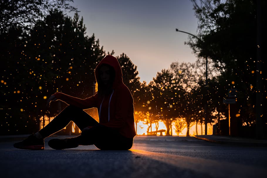 silhouette of woman sitting on road during golden hour, human