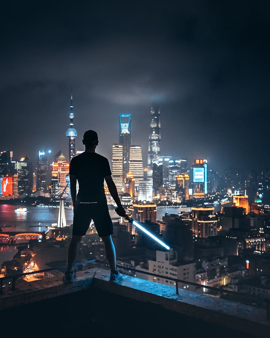 man holding lightsaber while standing on ledge overlooking city, HD wallpaper
