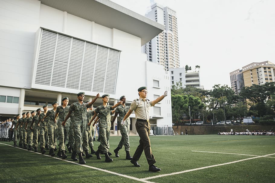 band of army marching on field beside buildings, person, human