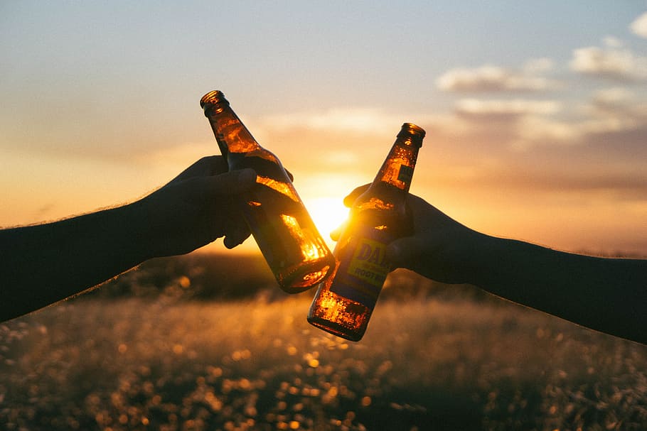 photography of person holding glass bottles during sunset, cheers