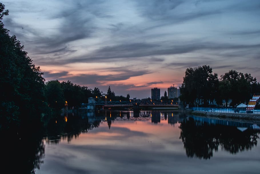 Calm Body of Water Near Tall Trees and Buildings With Pedestal Post Lights during Golden Hour