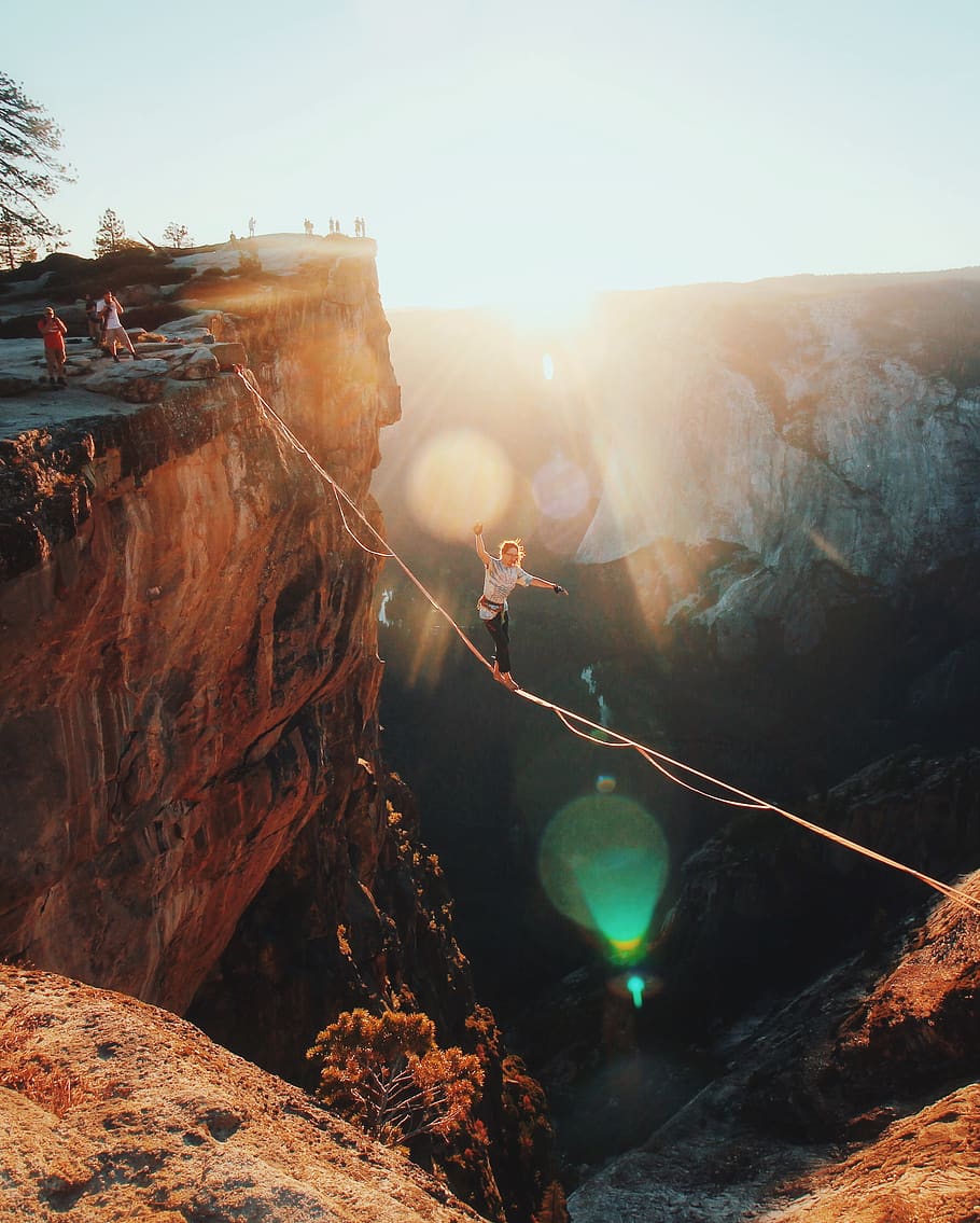 man walking on string hanging from rock mountains, lens flare HD wallpaper