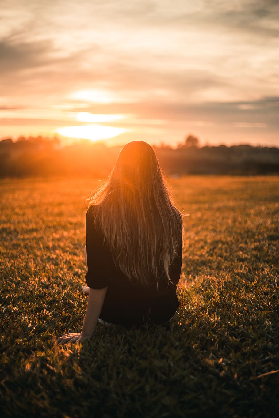 Woman in Black Shirt Sitting on Grass during Sunset, back view