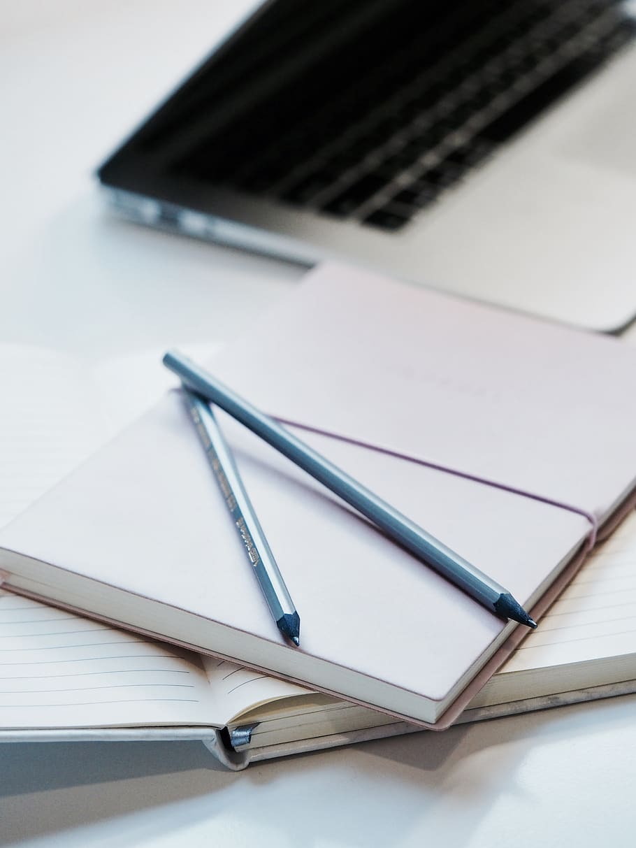 close-up photography of two pencils on closed pink covered book on desk near MacBook Air in a well-lit room, HD wallpaper