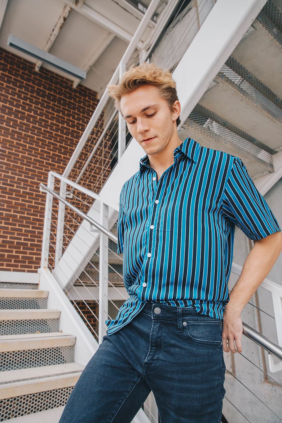 man in blue and black striped button up polo shirt and blue denim jeans staands on stairs