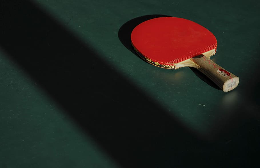 red and brown ping pong table on green panel, paddle, bat, shadow