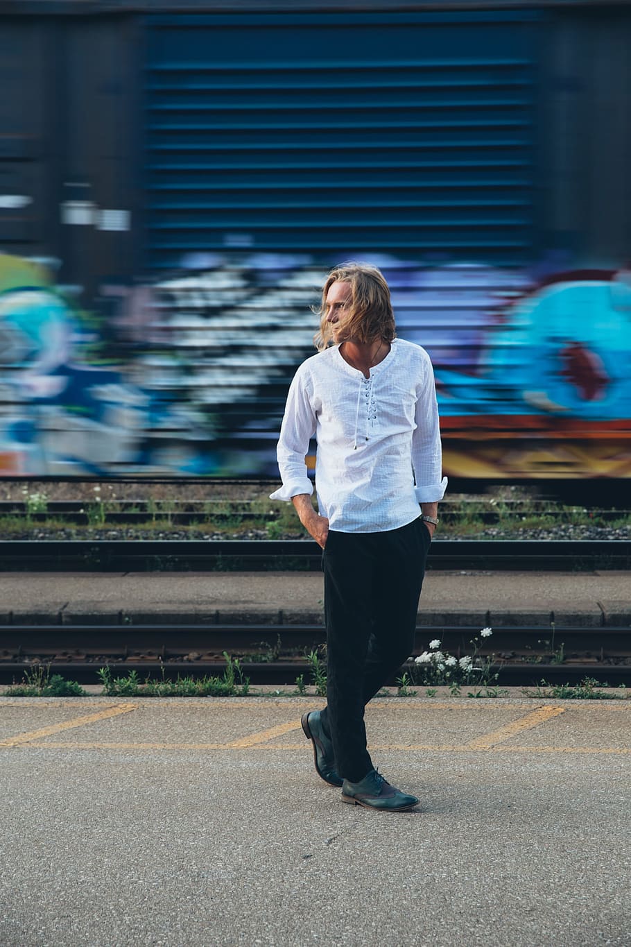 A fashionable man walks by train tracks with graffiti in the background