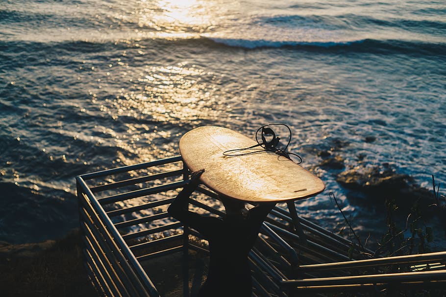 Person Carrying Brown Surfboard Near Body of Water during Golden Hour HD wallpaper