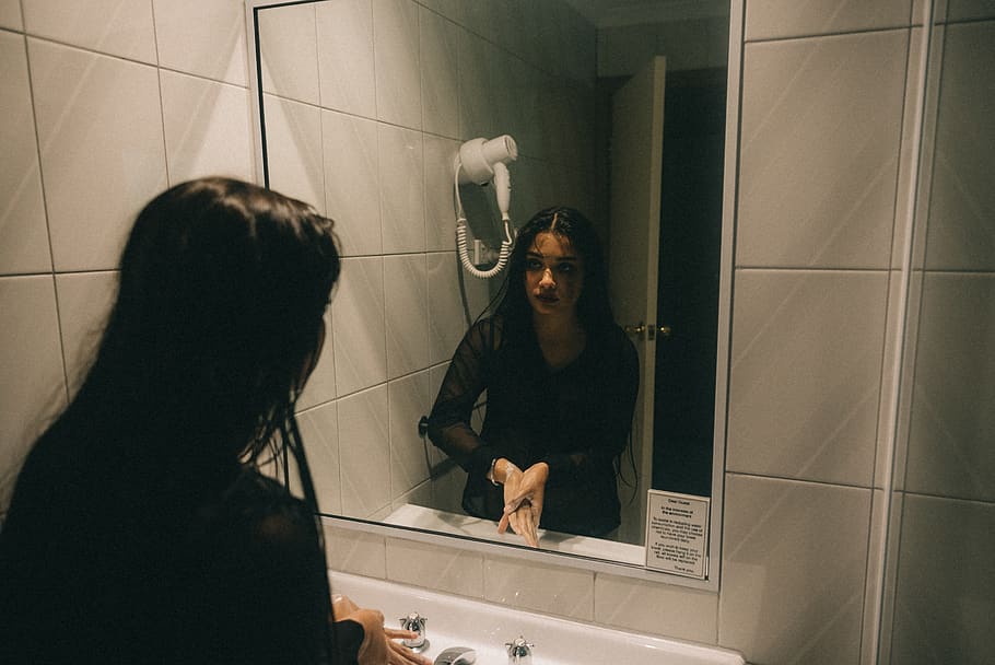 woman washing her hands while looking to the mirror, person, human