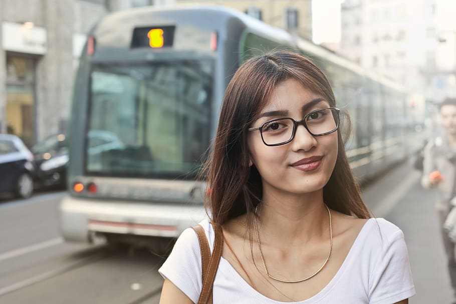 Young Asian Woman In White T-Shirt And Spectacles Standing Near Running Tram On The Road