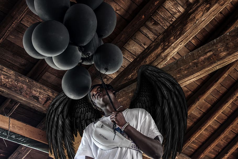 man wearing white shirt holding balloons with wings, black, african american