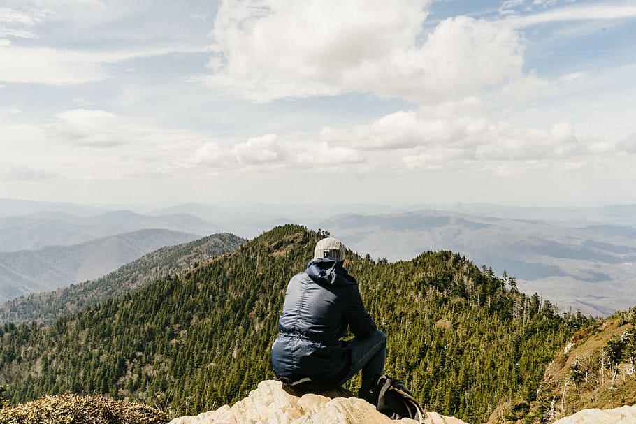 man sitting on mountain in front of trees under cloudy sky, rock HD wallpaper