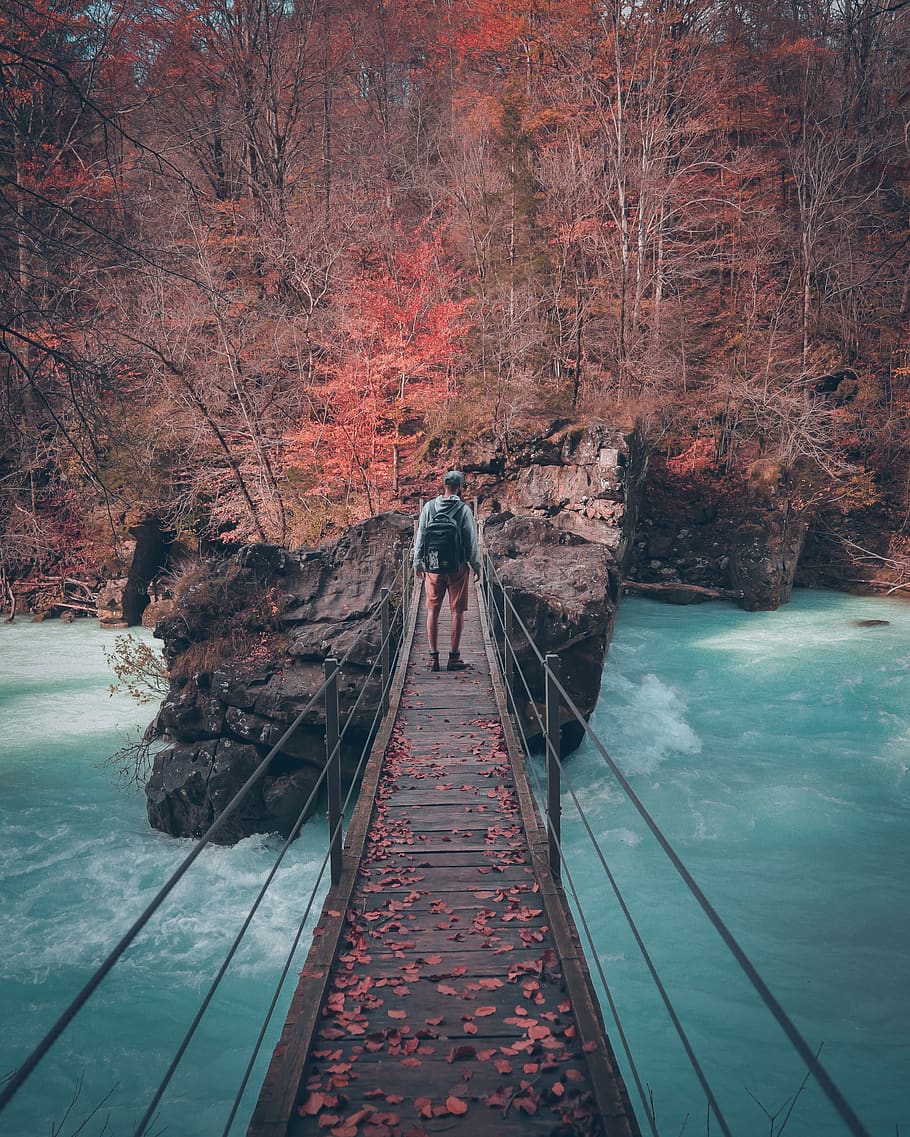 man on brown bridge near trees, building, person, human, suspension bridge