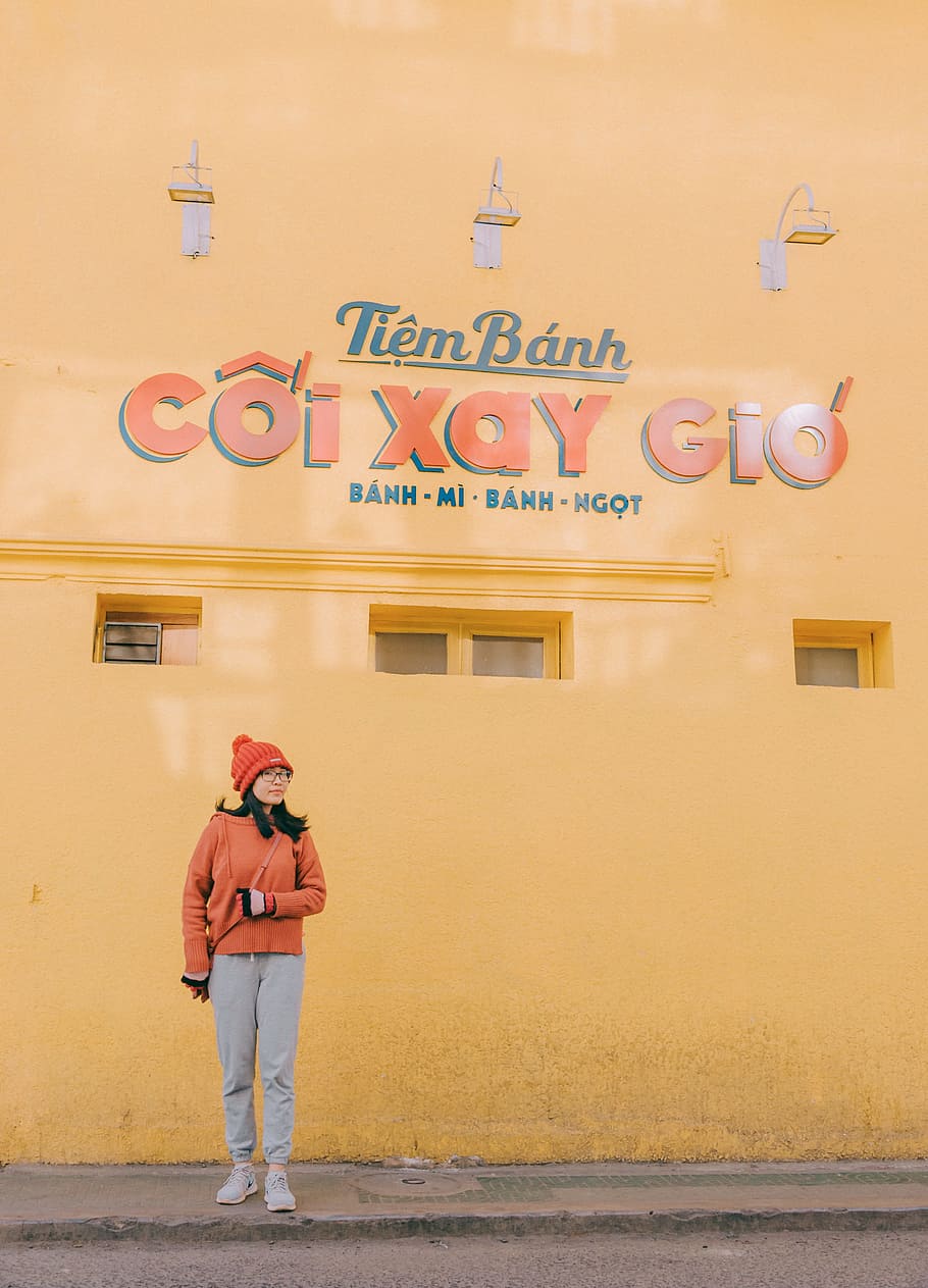Woman in Orange Sweater and Gray Pants Outfit Standing Near Tiem Banh Wall
