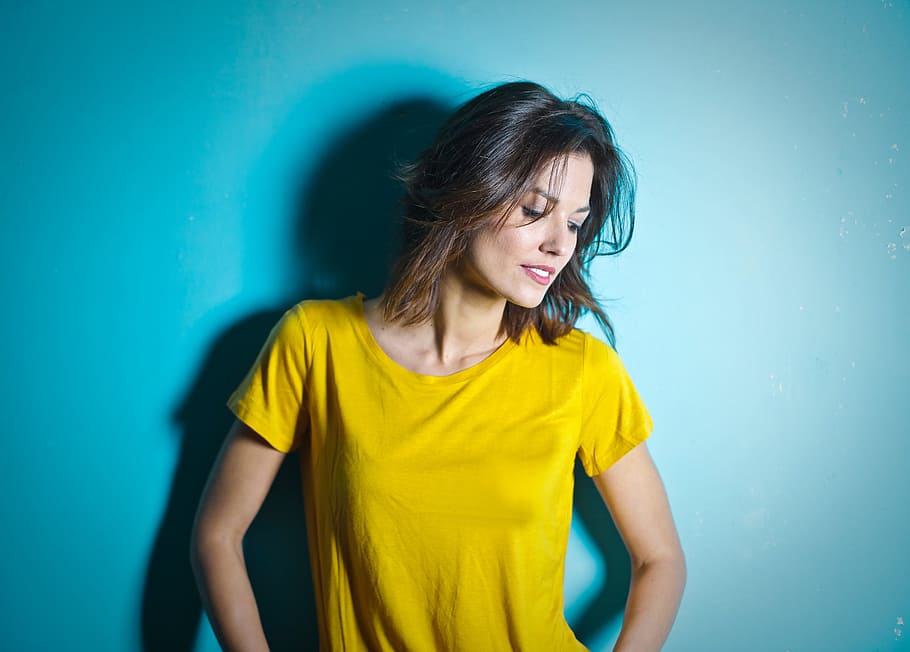 Young Woman Wearing Yellow Scoop Neck T-Shirt Posing Against Blue Wall
