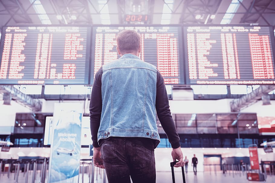 Young man with luggage checking flight timetable in international airport HD wallpaper
