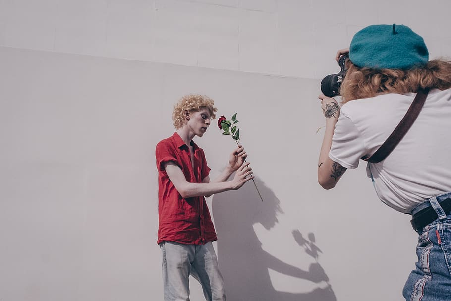 Woman Taking Photo of Man Standing and Holding Red Flower Near Wall HD wallpaper