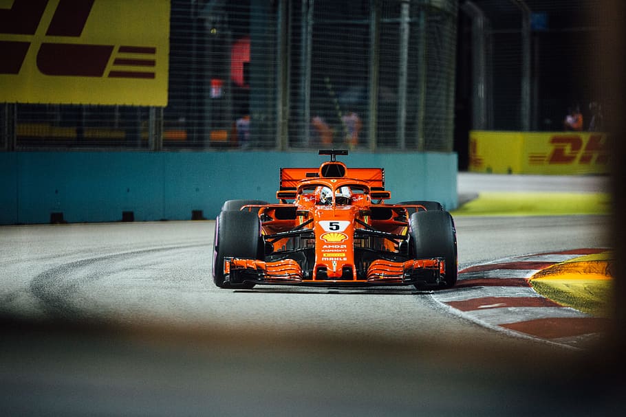 orange and black racing car near grey metal rails at daytime HD wallpaper