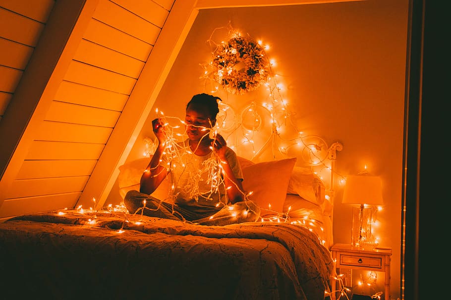 man sitting on bed surrounded by lighted yellow string lights HD wallpaper