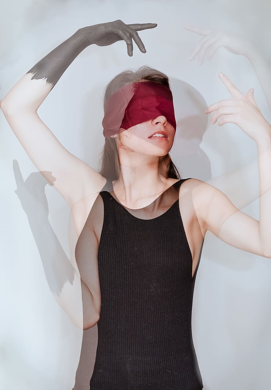 woman with red blindfold wearing black sleeveless top standing beside white wall