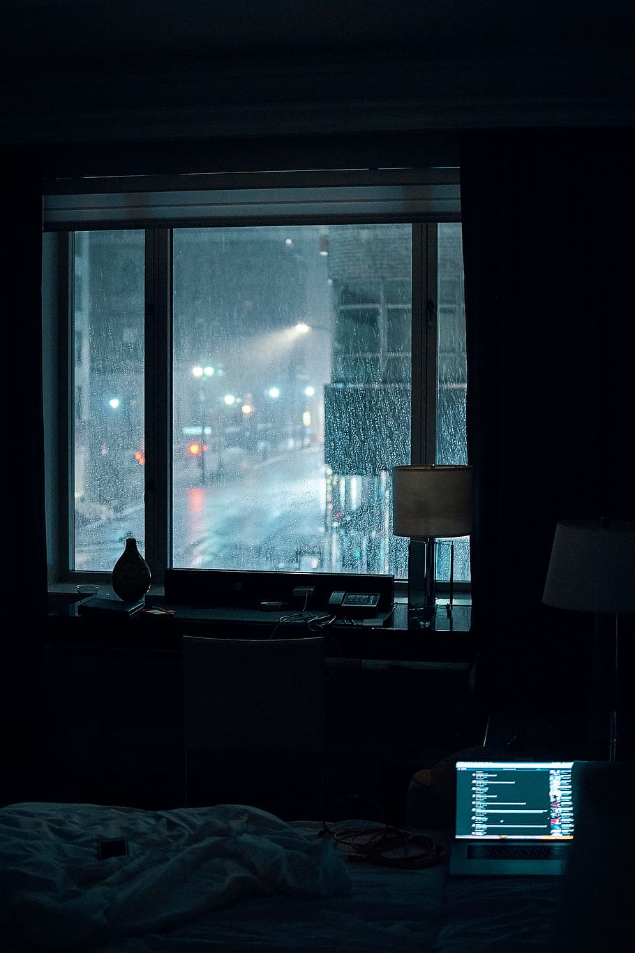 laptop computer left turned-on on bed inside room during rainy night