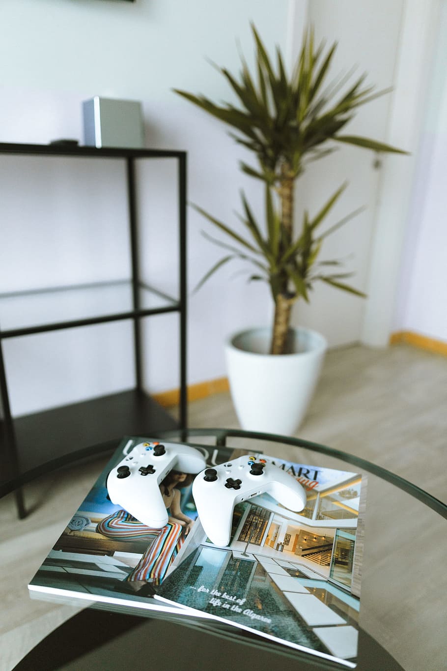two Xbox One game controllers on magazine book on top of glass table HD wallpaper