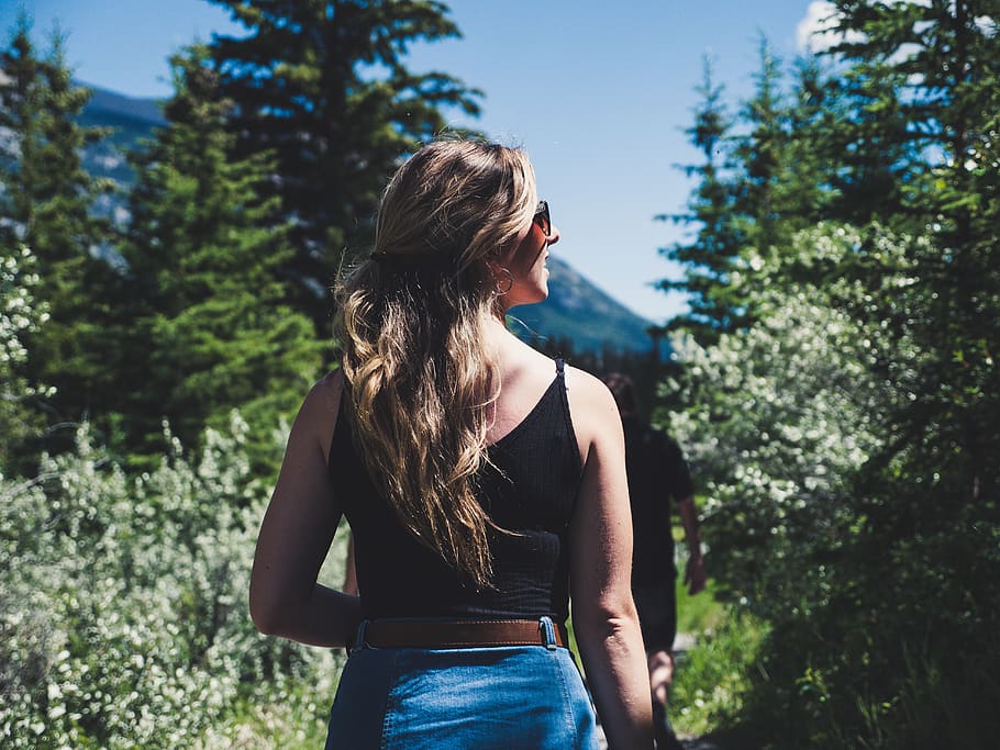 woman wearing black spaghetti strap crop top standing in front of trees while looking left side during daytime