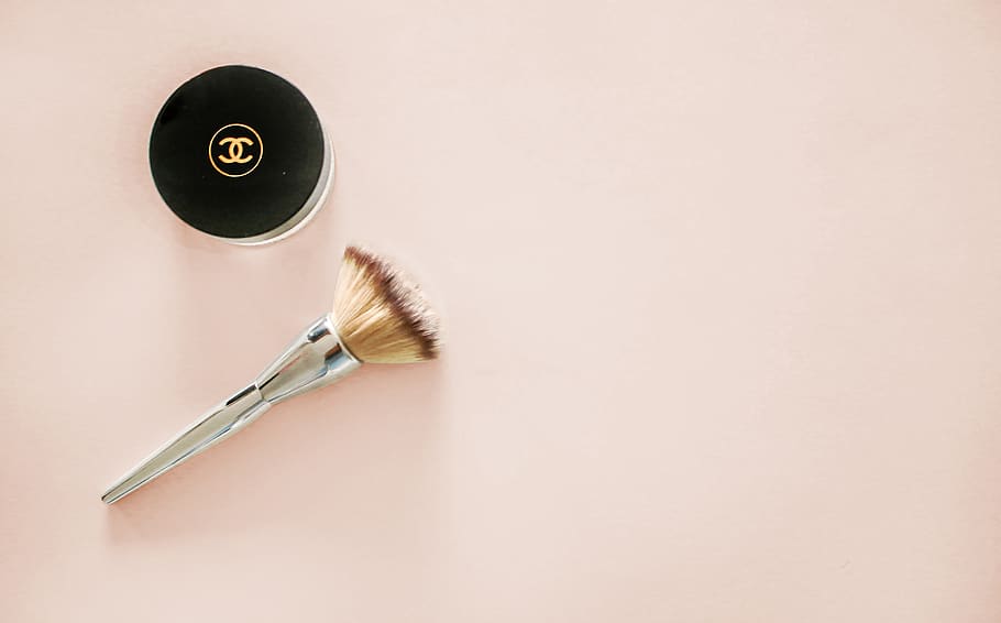 makeup brush and Chanel compact jar on beige surface, studio shot