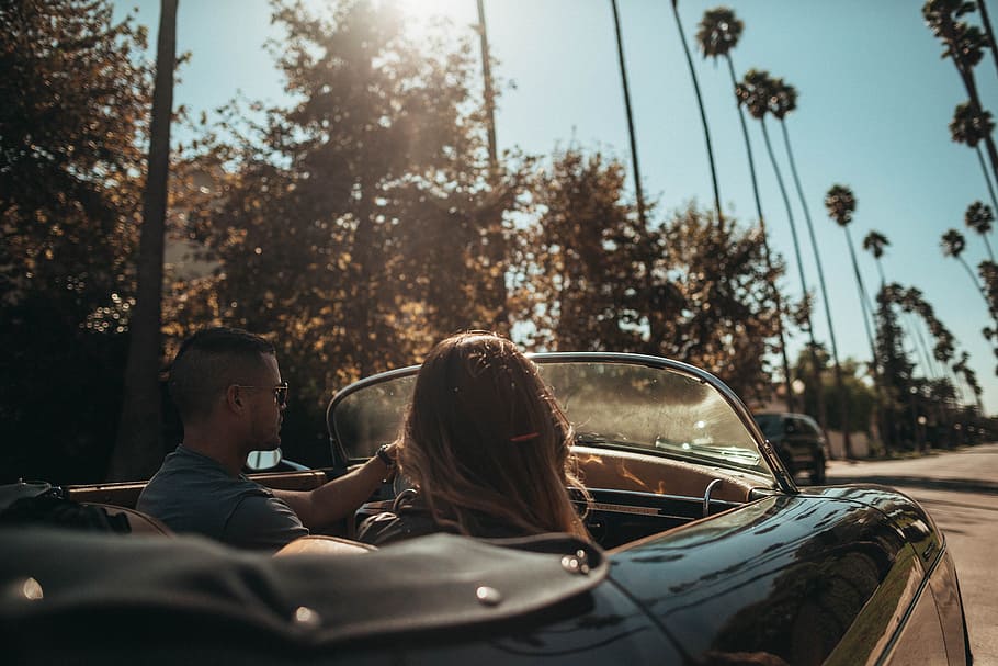 man driving convertible beside woman, car, tree, sunlight, outdoors