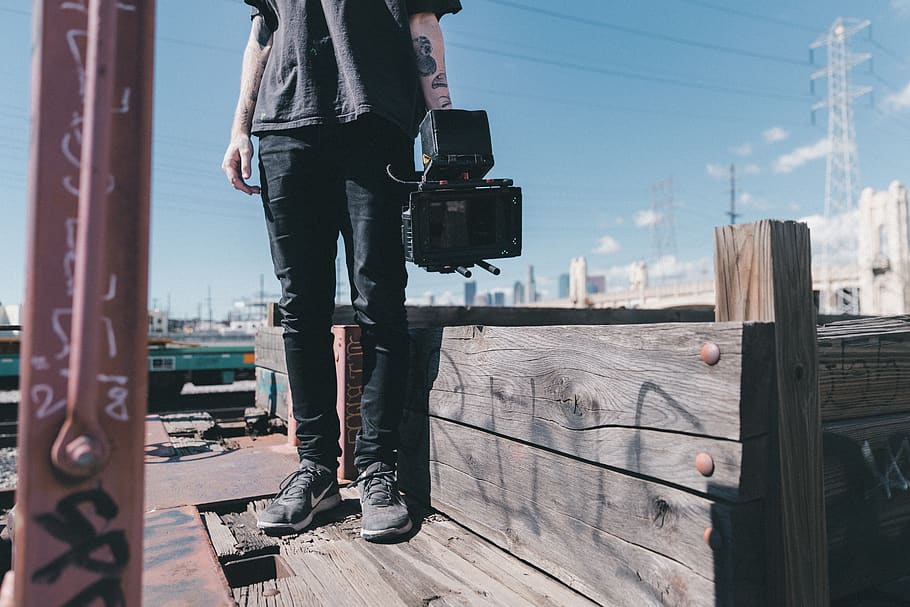 man holding black video camera while standing on plank, real people HD wallpaper