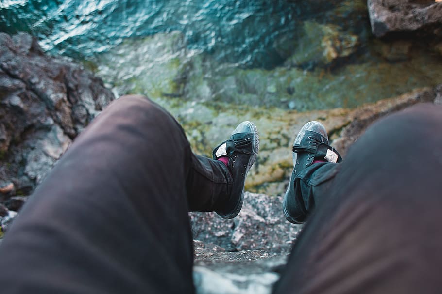 Feet hanging over the edge of a rock with blue sea water in the background HD wallpaper