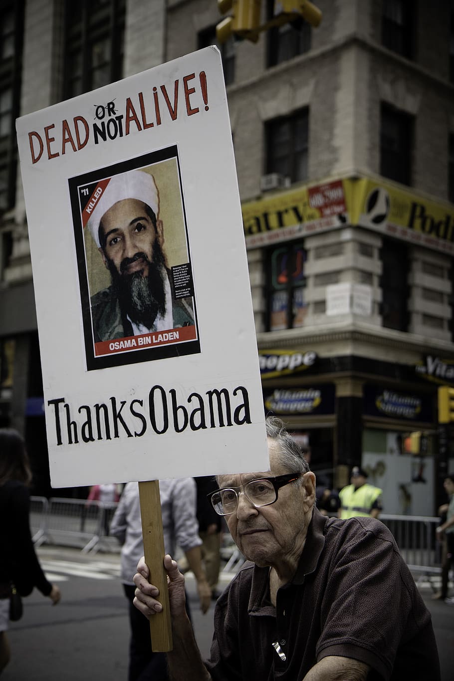 man sitting holding Dead Not Alive! Thanks Obama placard, person