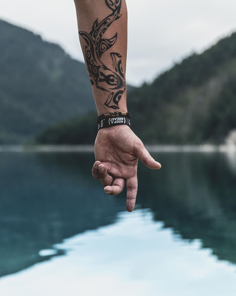 hand of person pointing to body of water with wrist tattoo, arm