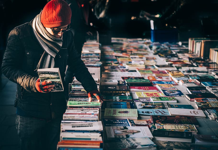 man picking up book ob book sale, guy, stall, market, scarf, hat, HD wallpaper
