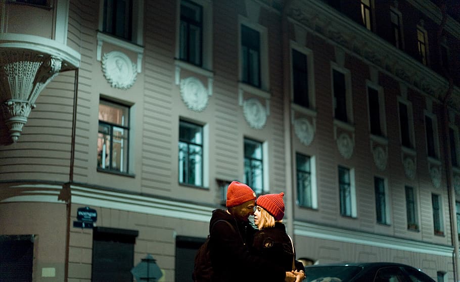 Man and Woman Wearing Red Knit Cap About to Kiss in Front of Gray Concrete Building during Nighttime HD wallpaper