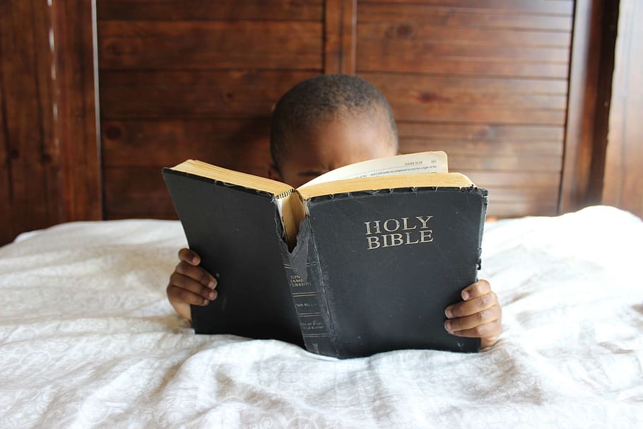 Photo of Child Reading Holy Bible, bed, book bindings, boy, furniture