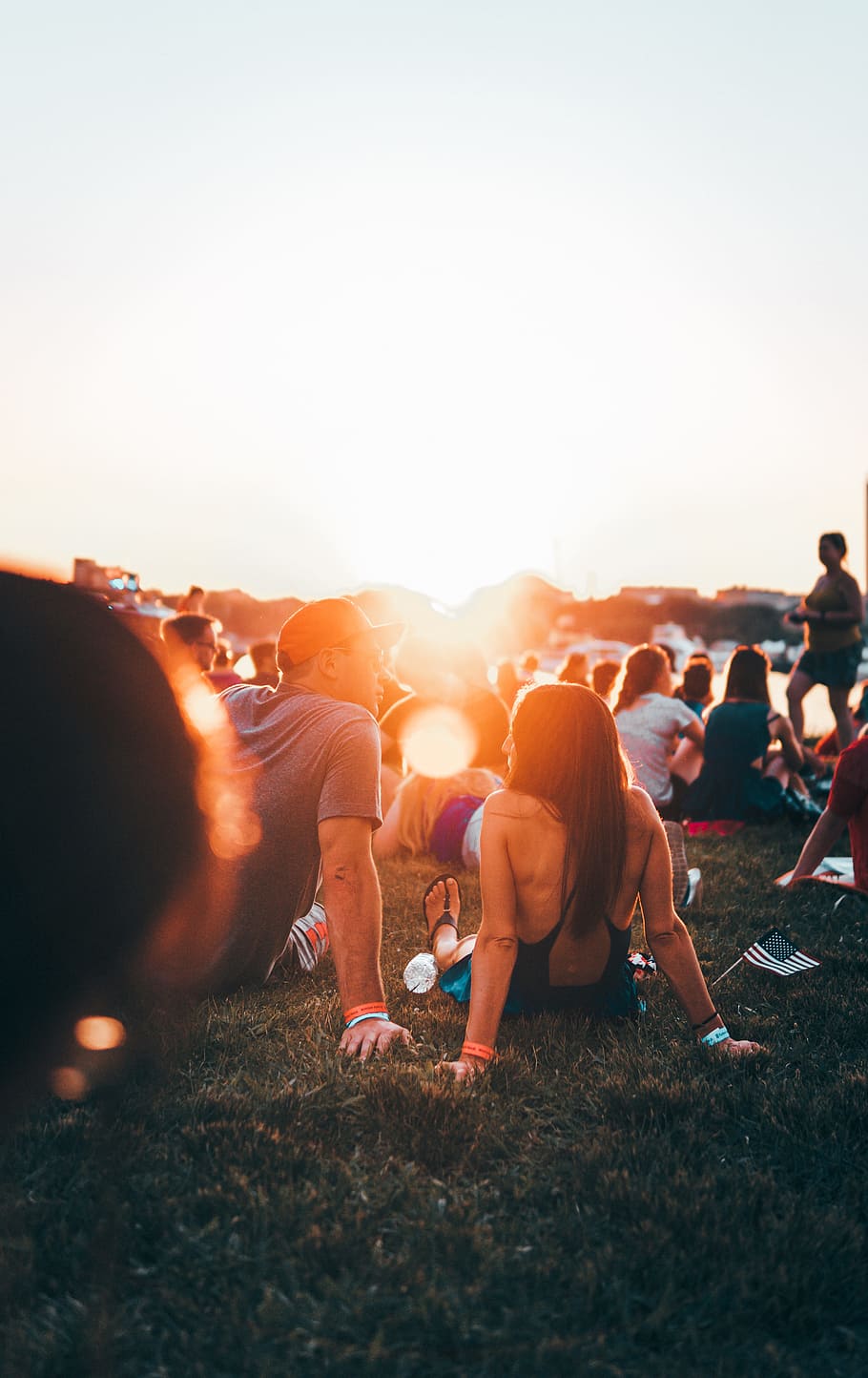 man and woman sitting on grass surrounded with people during golden hour HD wallpaper
